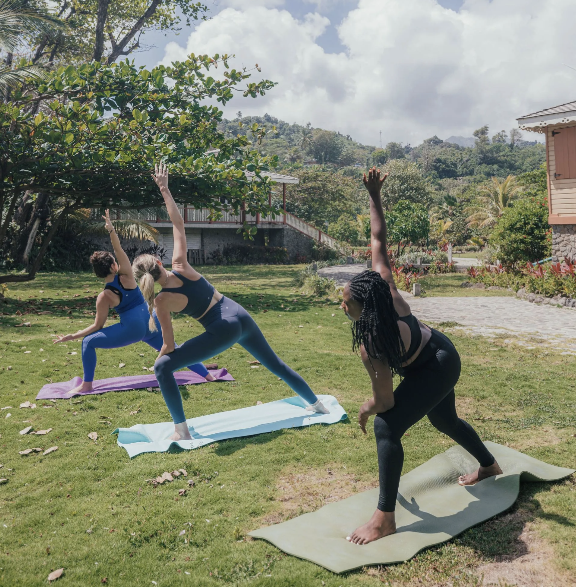 Three people practising yoga outdoors among tropical gardens