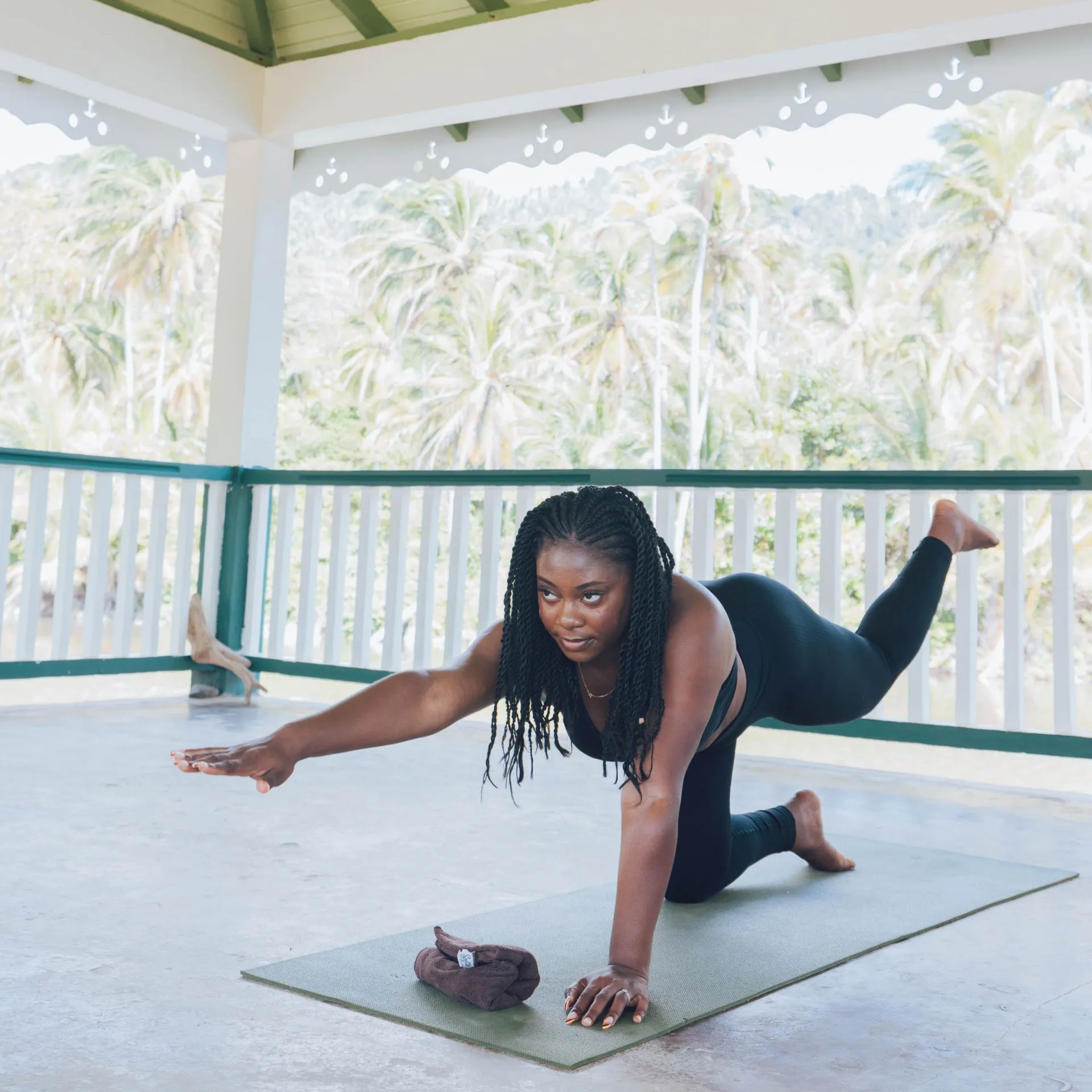A woman practising yoga on an open veranda surrounded by palms